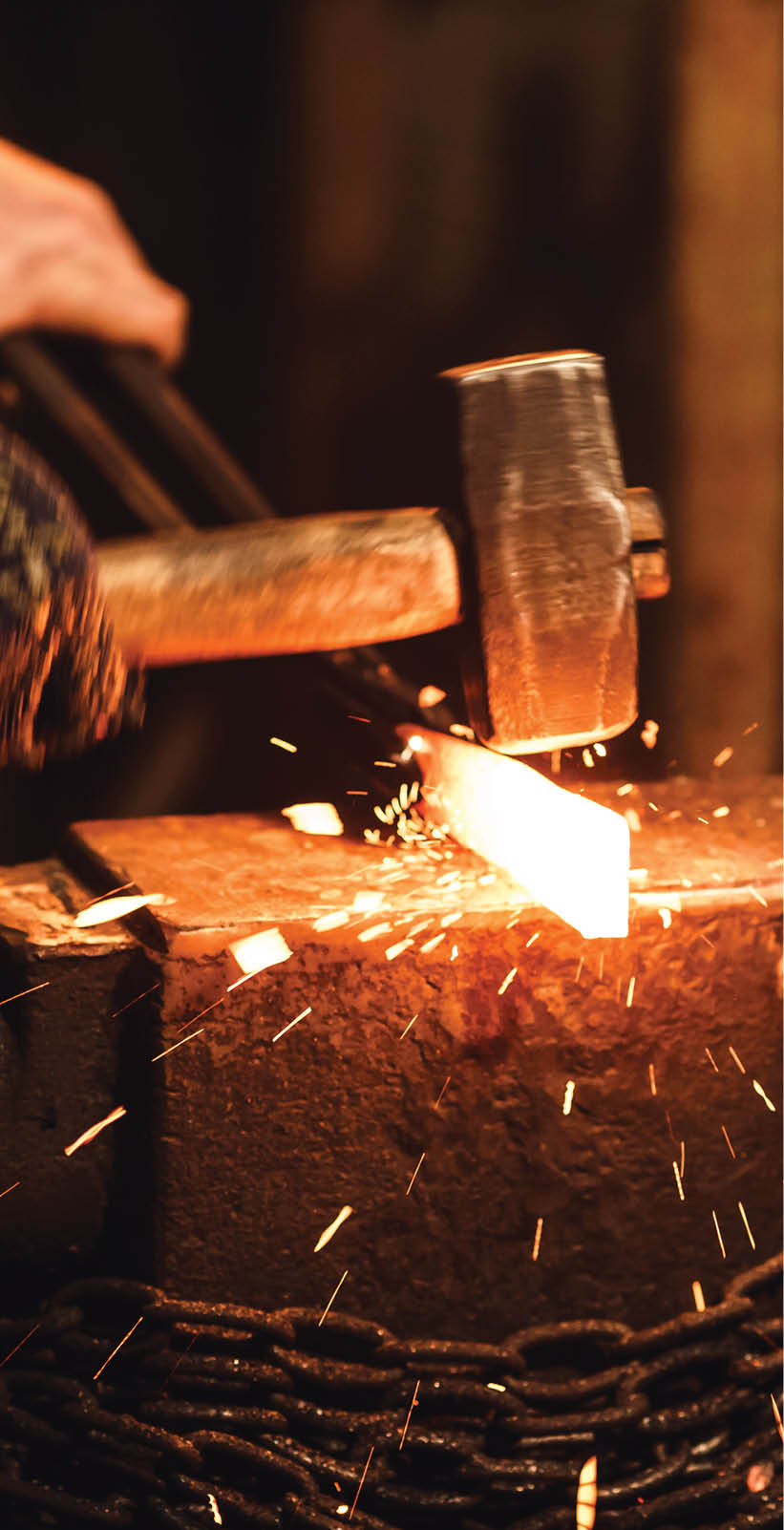 The blacksmith manually forging the red-hot metal on the anvil in smithy with spark fireworks