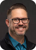 A man wearing a blue shirt and a black jacket. Description generated by AI
