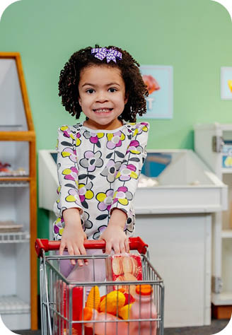 A little girl is pushing a shopping cart filled with groceries. Description generated by AI