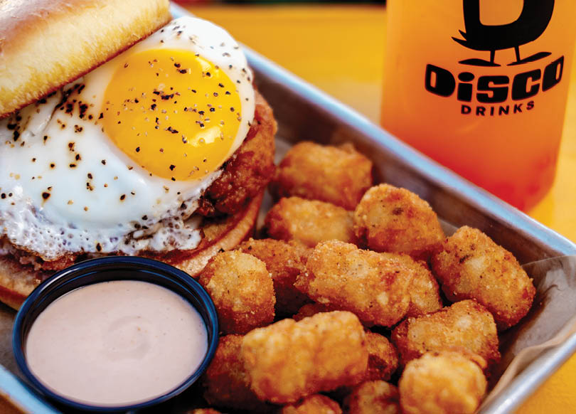 A sandwich with a fried egg on top and a side of tater tots. AI generated content