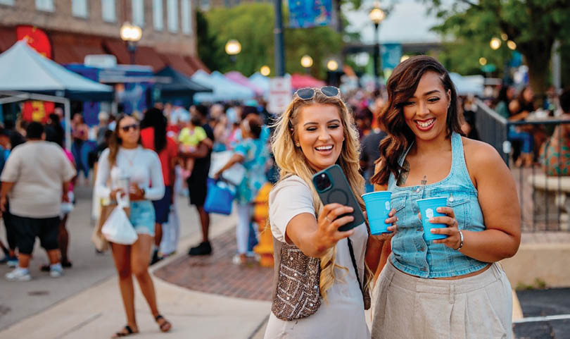 Two women taking selfies in a crowded street. Description generated by AI