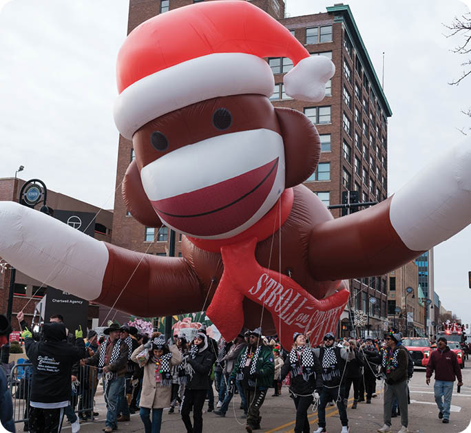 A large inflatable monkey balloon is being carried by a crowd of people down a street. AI generated content