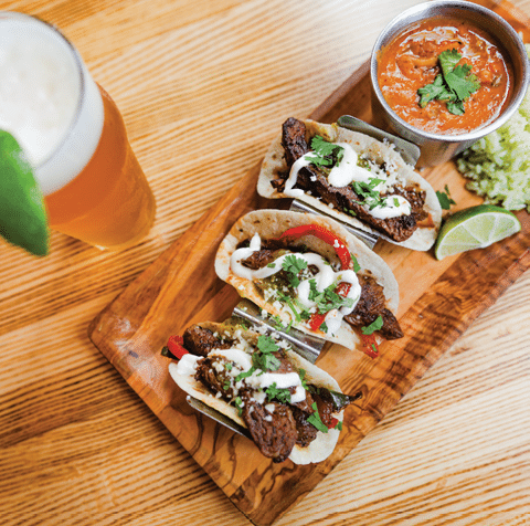 A wooden tray with 5 tacos and a bowl of salsa. AI generated content