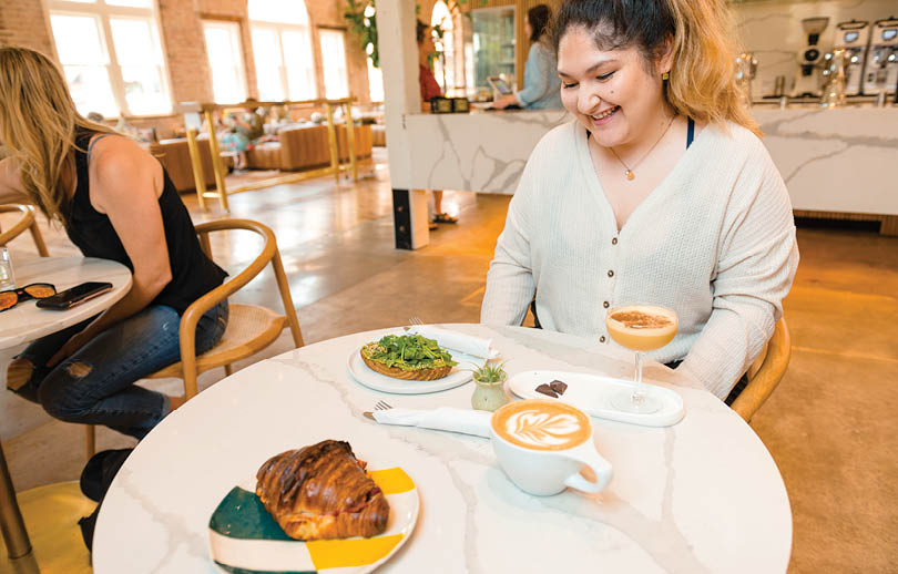 A woman is sitting at a table with a plate of food and a cup of coffee. AI generated content