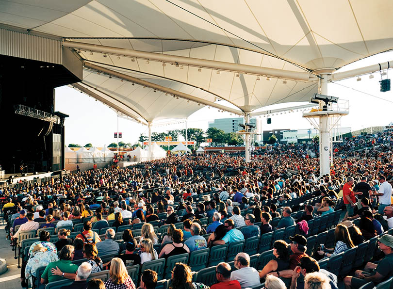 A large crowd of people are sitting in the bleachers, watching a concert. AI generated content