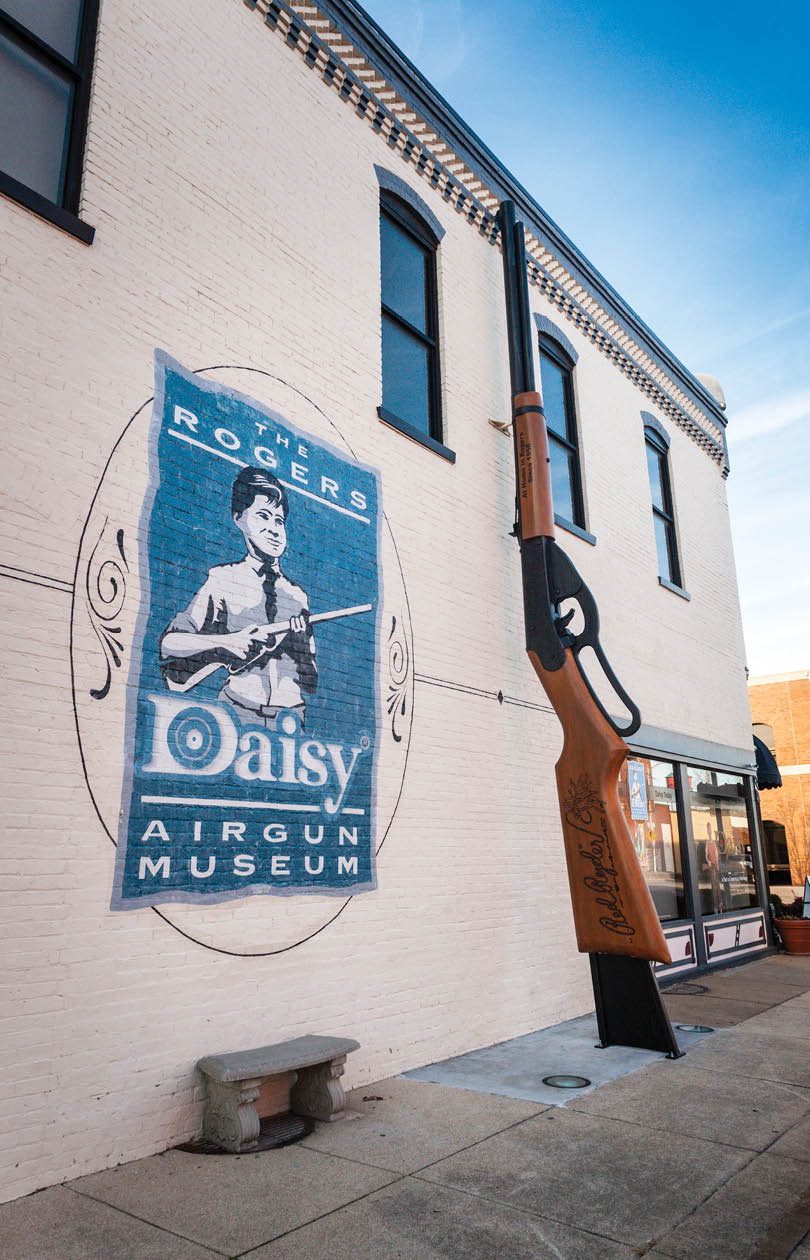 A statue of a man holding a rifle is displayed in front of a building. AI generated content