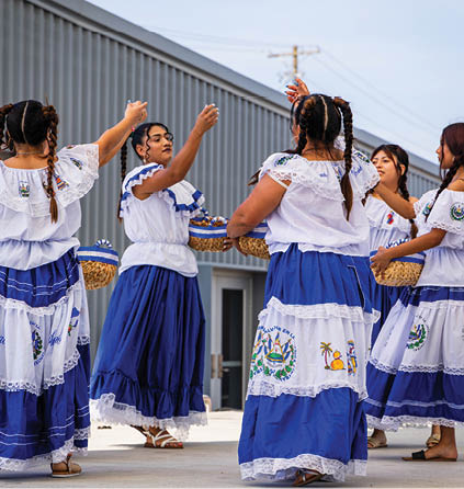 A group of women in traditional Mexican dresses are dancing in front of a building. AI generated content