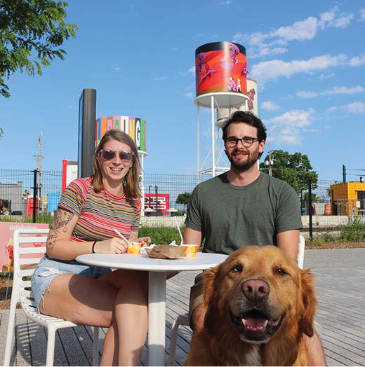 A man and woman sit at a table with a brown dog. AI generated content