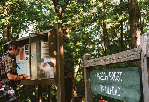A man is standing next to a sign that says “Pigeon Roost Trailhead." AI generated content