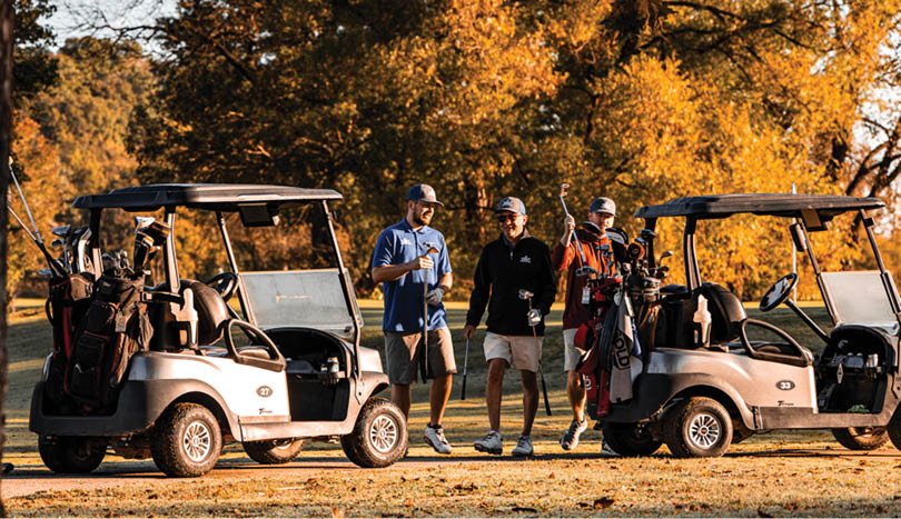 Four golfers standing next to their golf carts. Description generated by AI