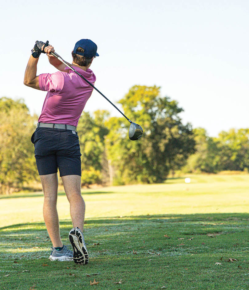 A man in a pink shirt is swinging a golf club. Description generated by AI