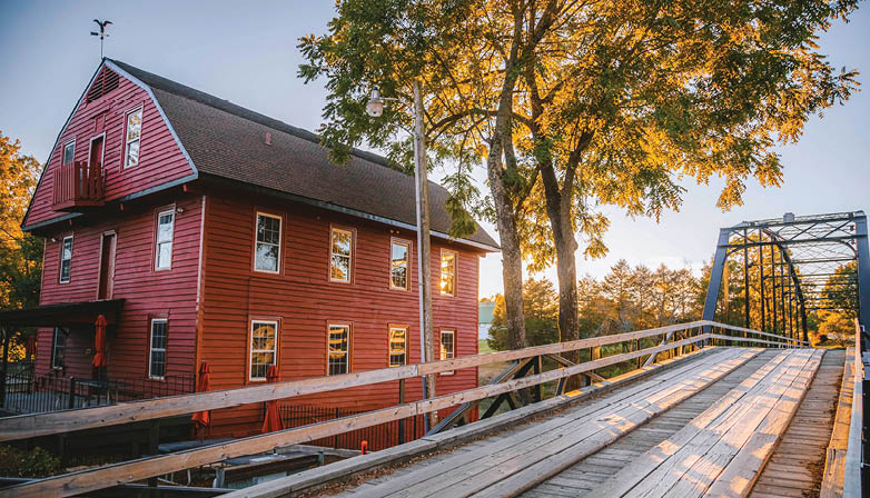A red house with a white roof is situated next to a bridge. AI generated content