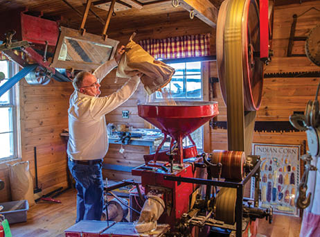 A man is pouring a bag of grain into a red machine. AI generated content