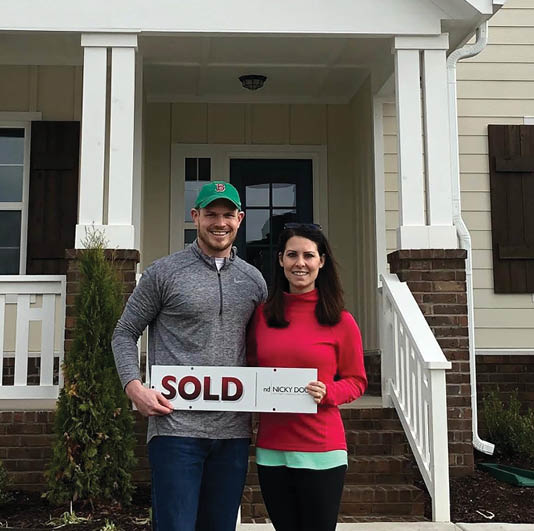 A man and woman standing in front of a house with a sold sign. Description generated by AI