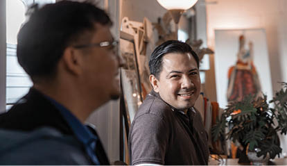 A group of people are standing outside, smiling and posing for a picture. There are several potted plants in the background, and a wine glass is visible in the foreground. AI generated content