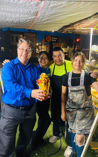 Three people are standing together, with one of them holding a food item. They are all smiling, and the food item appears to be a dessert. AI generated content