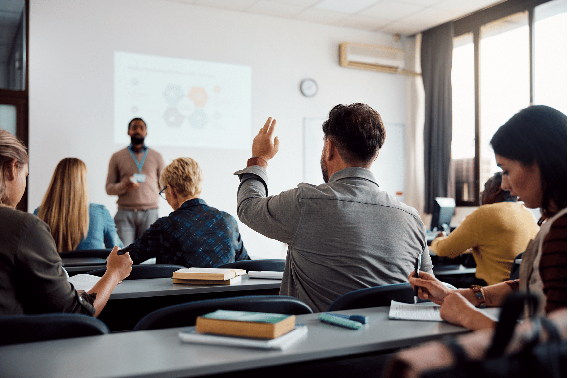 Rear view of man raising arm to ask a question during a presentation in lecture hall.