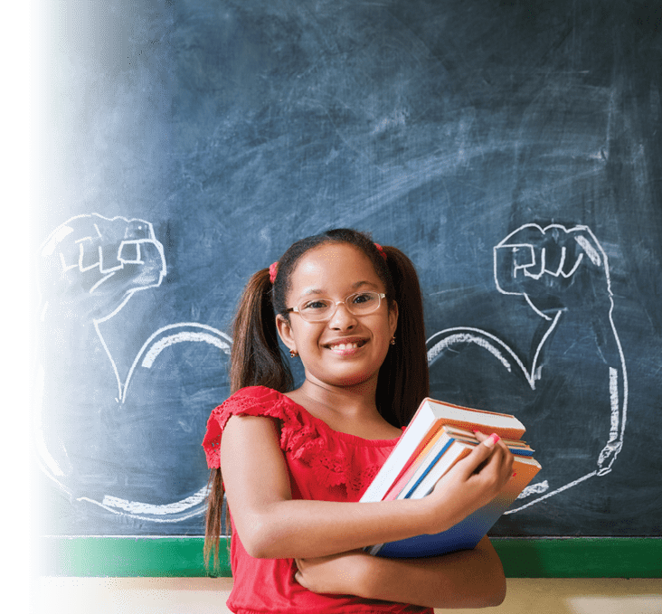 Concept on blackboard at school. Intelligent and successful hispanic girl in class. Portrait of female child smiling, looking at camera, holding books against drawing of muscles on blackboard