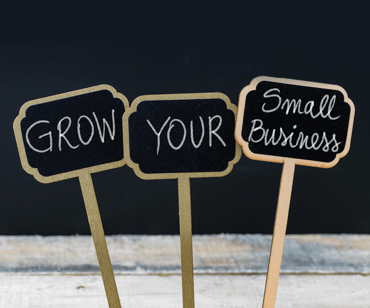 GROW YOUR SMALL BUSINESS message written with chalk on wooden mini blackboard labels, defocused chalkboard and wood table in background