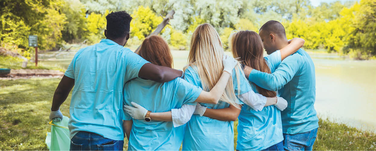 Volunteering, people and ecology concept. Group of volunteers embracing in park, back view, copy space