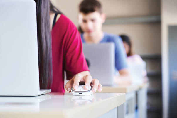 Close-up of a hand clutching a mouse in a high school classroom, a group of cheerful students study with a laptop computer. Concept of technology and education. High quality photo