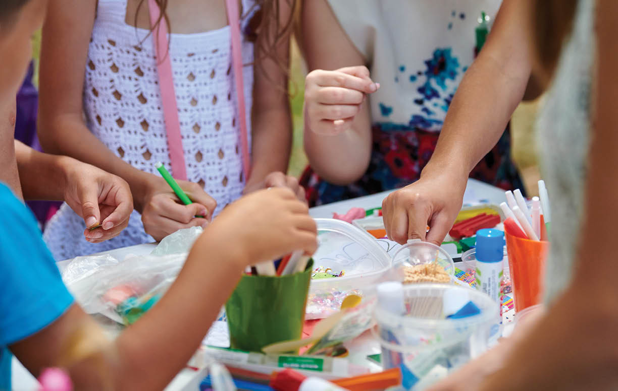 Children paper crafting with parents in outdoor children party, painting, molding of plasticine and making figures cut from paper. Children hobby paper craft modeling, group development of children
