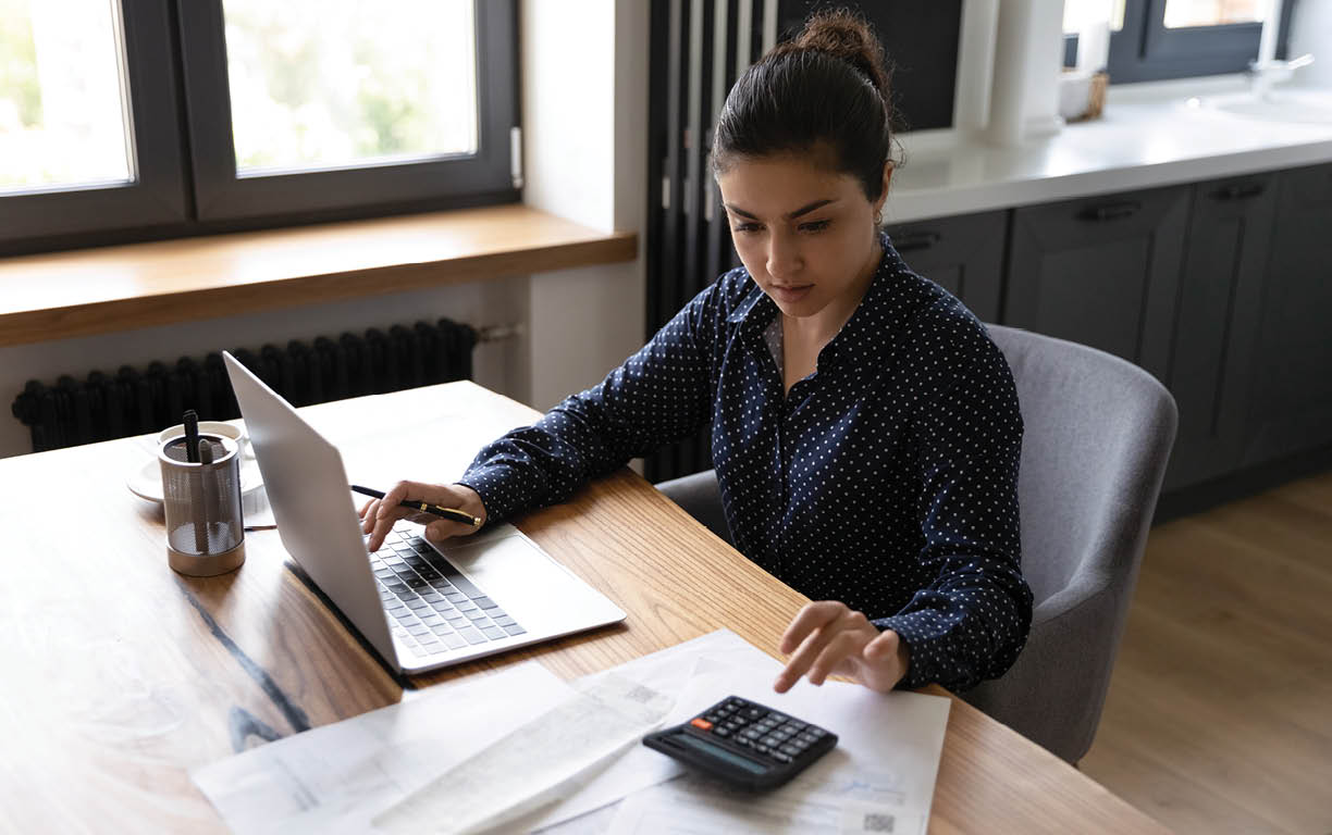 Bookkeeping. Busy millennial indian woman professional accountant preparing annual financial report checking result on calculator. Mixed race female freelancer counting tax rates declaring income