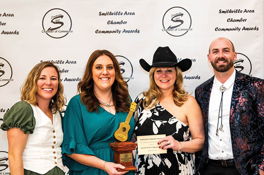 Three women and a man pose with a guitar trophy. AI generated content