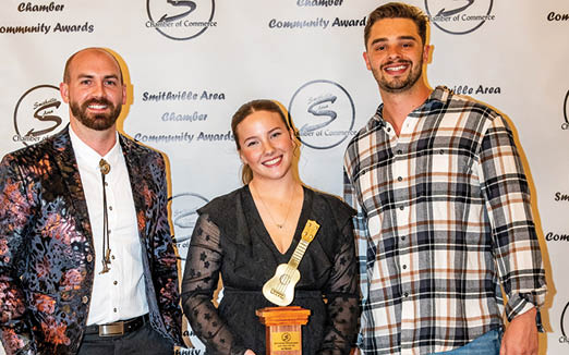 Three people pose for a photo, with a woman holding an award in the middle. AI generated content