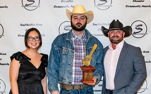 A man in a cowboy hat holds a trophy while standing next to a woman and another man. AI generated content