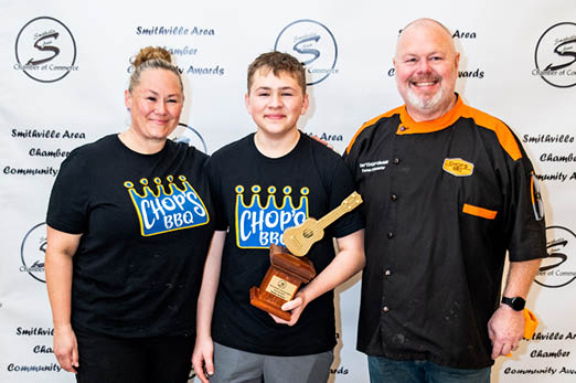 A man, woman, and boy are standing in front of a backdrop. The boy is holding a trophy. AI generated content