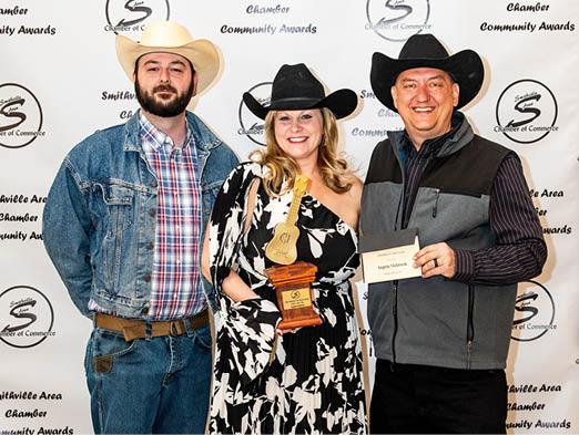 A man and two women pose for a photo, with one of the women holding an award. AI generated content