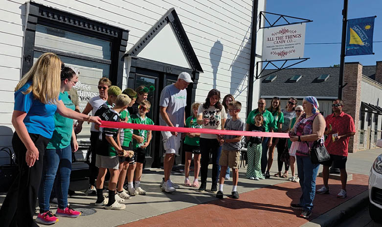 A group of people are gathered in front of a building, with a man holding a red ribbon. A woman is holding a pair of scissors, ready to cut the ribbon. AI generated content