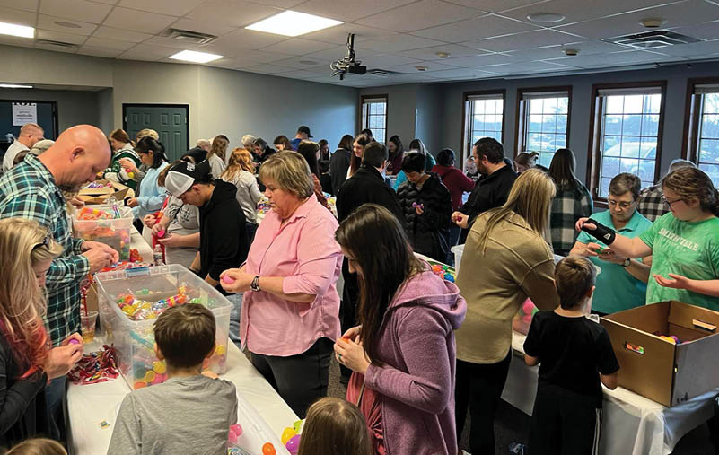 A large group of people are gathered in a room, making crafts and decorating eggs. AI generated content