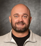 A man with a beard and mustache is wearing a gray sweatshirt with a logo on the front. AI generated content