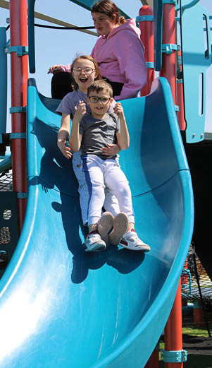Three children are sitting on a blue slide, enjoying their time at the playground. AI generated content