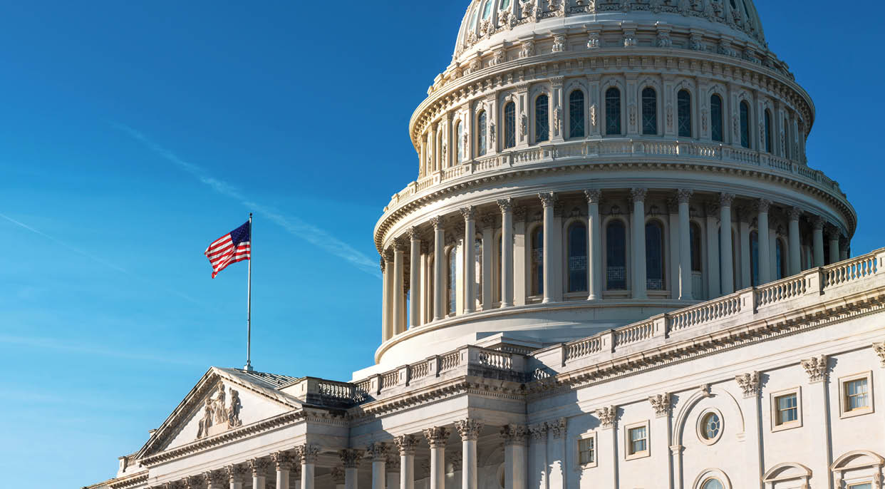 Panoramic view of the United States Capitol dome with its flag against a blue sky.