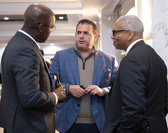 Three men in suits are standing together, talking and enjoying a beer. AI generated content
