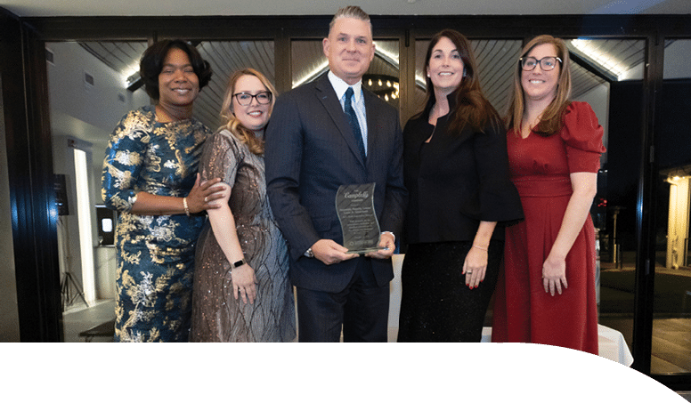 A group of four women and a man stand on a stage, with the man holding an award. AI generated content