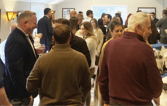 A group of people are gathered in a room, socializing and enjoying each other's company. There are several cups and bowls scattered throughout the room, suggesting that the gathering may be a casual event or party. A man is pouring coffee into a cup, and a blender can be seen in the background. The room appears to be a mix of indoor and outdoor elements, with a ceiling fan and a window visible. AI generated content