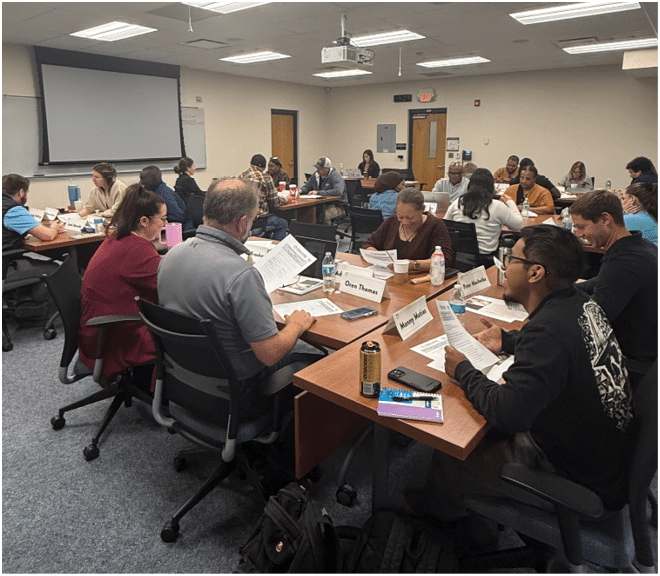 A group of people are sitting around a table in a classroom setting, working on papers. AI generated content
