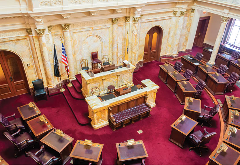 A large room with a wooden desk and chairs. The desk is covered with papers and books. There are several chairs around the desk, some of which are empty. A flag is hanging from the ceiling. AI generated content