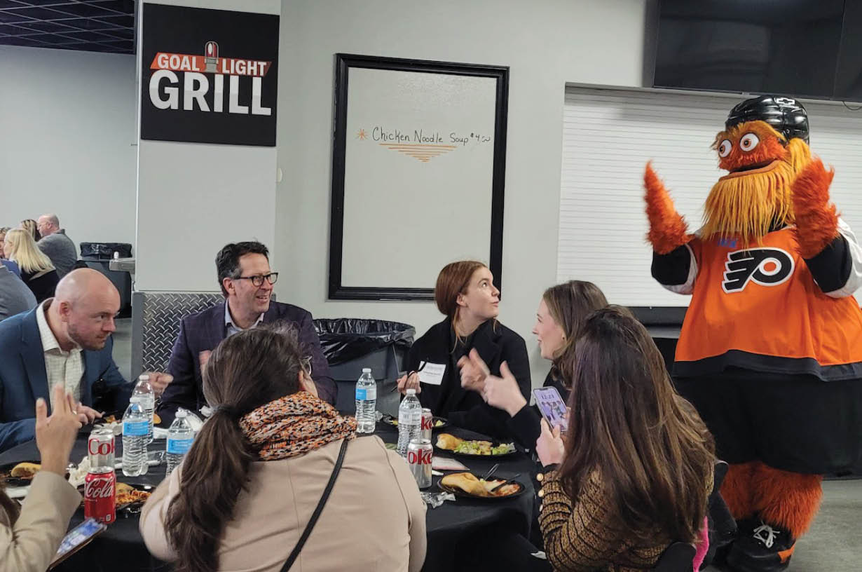 A group of people are sitting around a table with a mascot in an orange and black costume. AI generated content