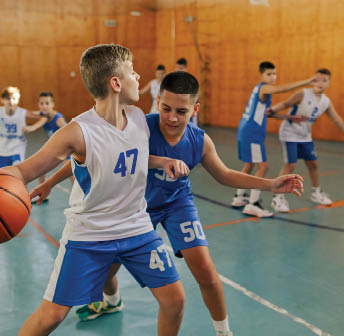 A young basketball players in action are practicing basketball at indoor court during the training. Dynamic picture of a basketball kids practicing moves and game tactics during the game on training.