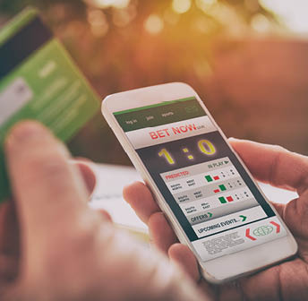 Man betting on sports with credit card, over shoulder view on hand with smartphone