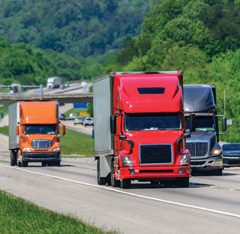 A steady flow of semis lead the way down a busy interstate highway in Tennessee. Heat waves rising from the pavement give a nice shimmering effect to vehicles and forest behind the lead trucks.  Excellent reverse copy space across both top and bottom of image.