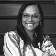 A person with long straight hair wearing glasses and a striped shirt is sitting in front of a wooden background. Description generated by AI