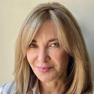 Person with shoulder-length straight blonde hair wearing a light-colored collared shirt against a plain background. Description generated by AI