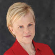 A person with short light hair wearing a red collared shirt stands with arms crossed against a dark background. Description generated by AI