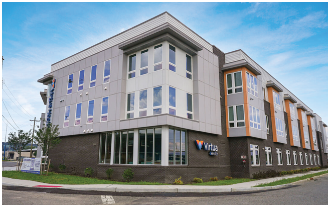 A modern three-story building with large windows and a sign reading Virtua Health is situated on a street corner under a blue sky. Description generated by AI